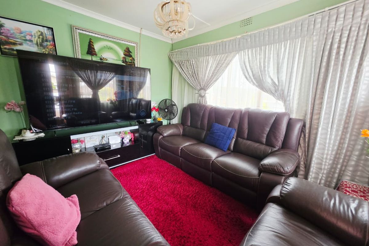 A cozy living room featuring a decorative ceiling rose, chandelier, and large window with curtain tracks, providing a comfortable space for relaxation.