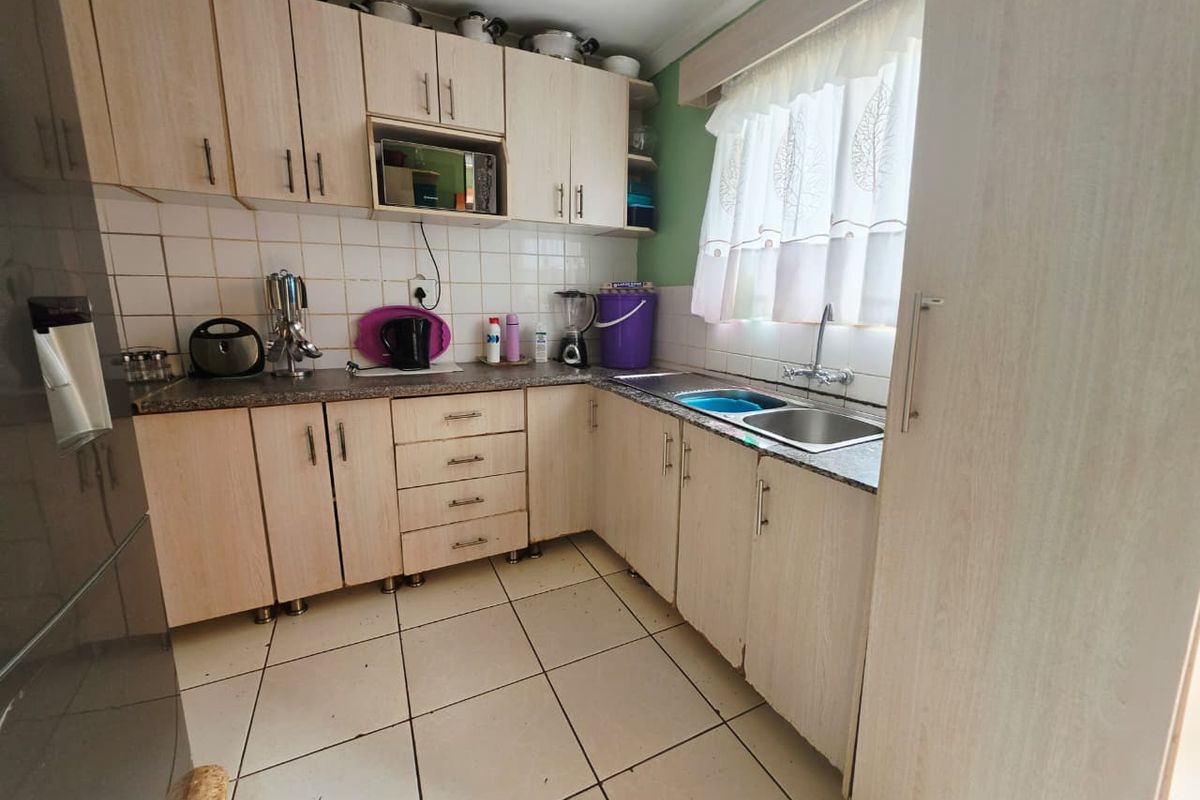 A functional kitchen featuring light wood-tone cabinetry, laminate countertops, a double basin sink, and tiled flooring, offering a practical layout for daily use.