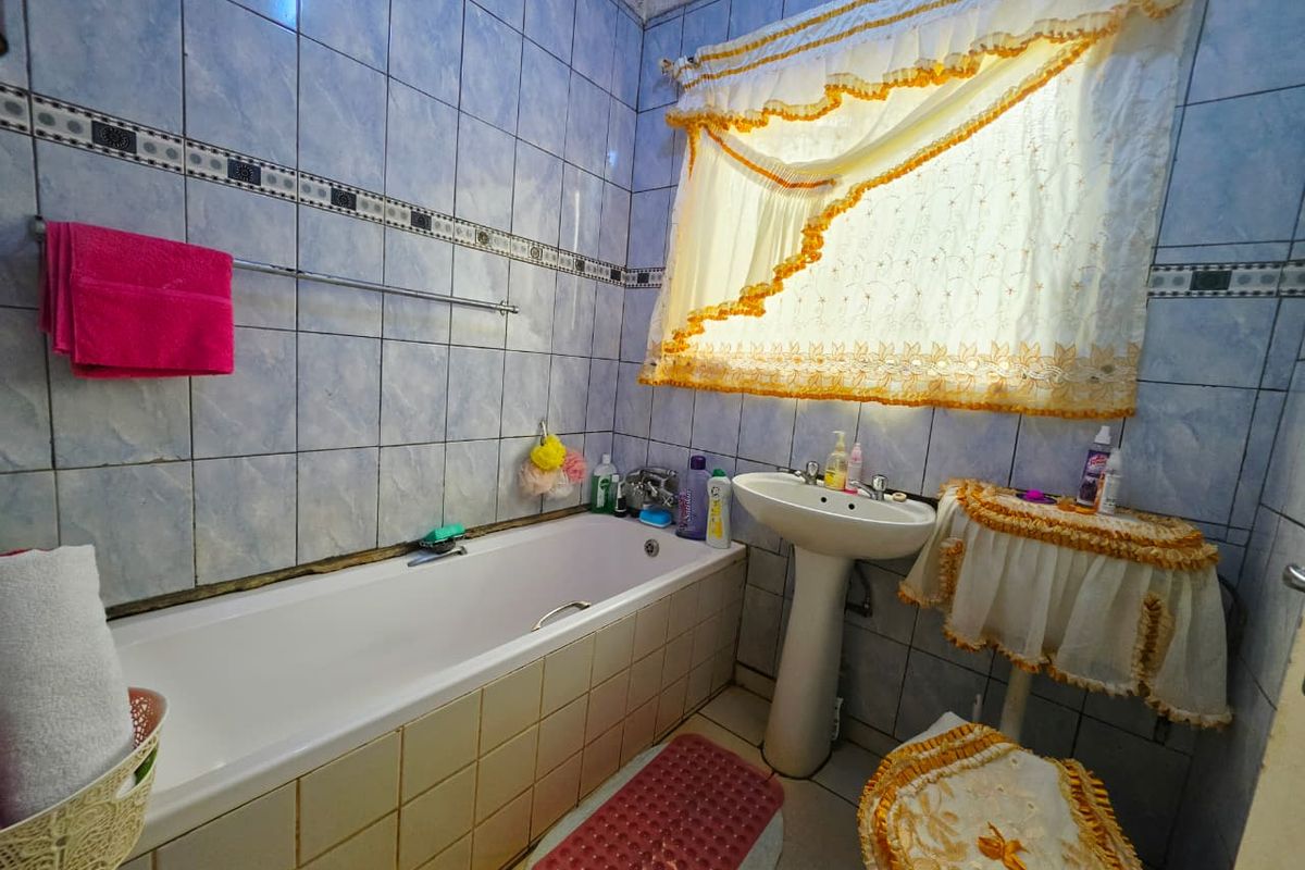 A dated bathroom featuring a bathtub and pedestal basin with full-height wall tiling and a window.