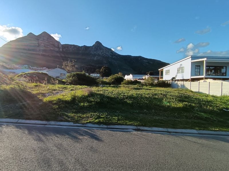 A vacant residential plot featuring a gentle slope, street frontage, and scenic mountain views in a developing neighborhood.