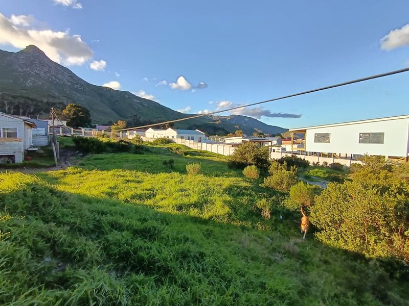 A view of a vacant residential plot featuring natural vegetation, perimeter fencing, and surrounding mountain scenery.