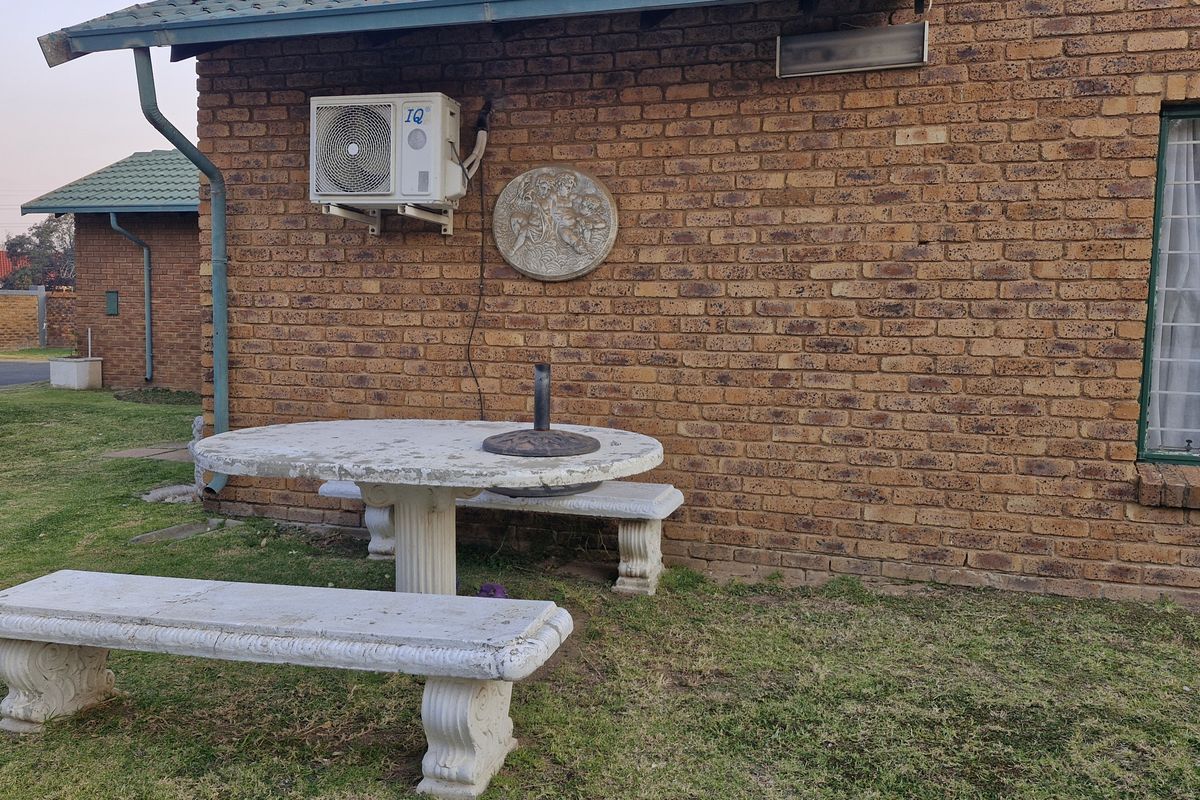 A rear exterior view of a brick house featuring an installed air conditioning unit and security bars on the window.