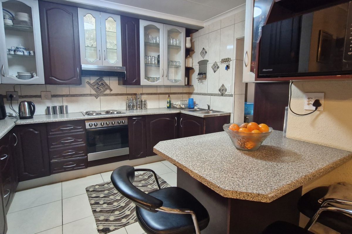 A functional kitchen featuring dark wood cabinetry, laminate countertops, a breakfast bar, and integrated appliances with tiled backsplash and flooring.
