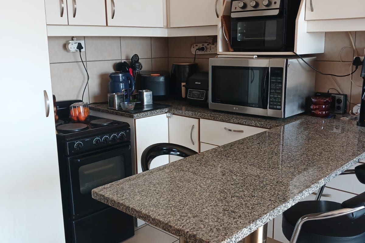 Compact kitchen featuring granite countertops, a breakfast bar, built-in cabinetry, and ceramic floor tiles, offering a functional layout for daily use.
