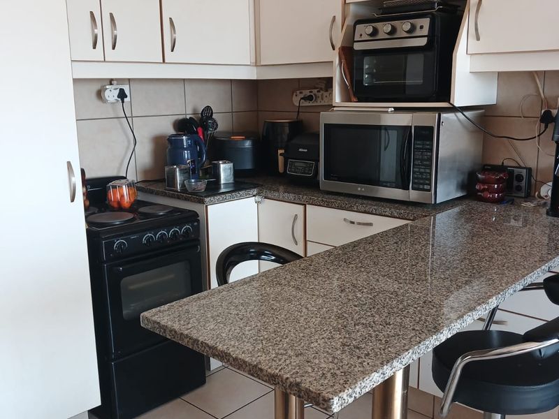 Compact kitchen featuring granite countertops, a breakfast bar, built-in cabinetry, and ceramic floor tiles, offering a functional layout for daily use.