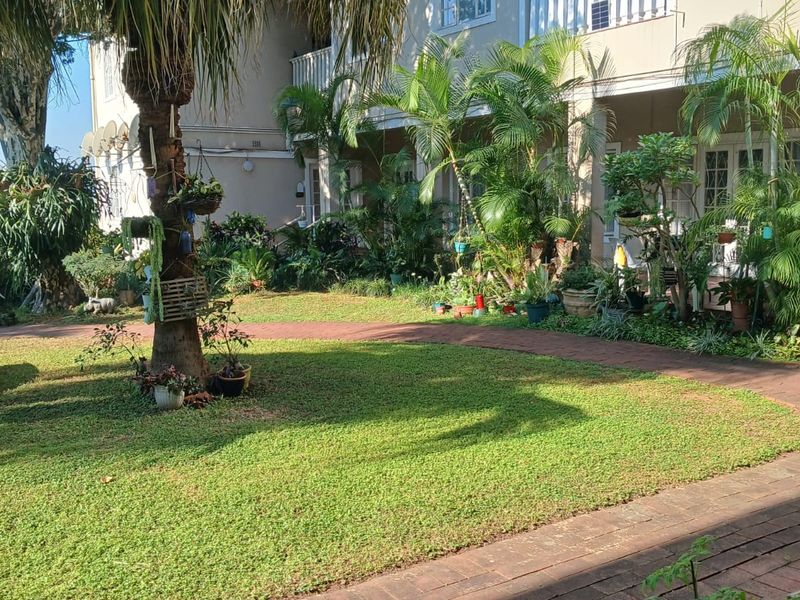 A well-maintained rear garden area featuring a brick paved pathway and access to apartment balconies.