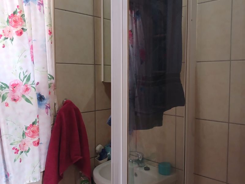 A compact bathroom featuring a pedestal basin, shower enclosure, and neutral wall tiling, currently requiring minor maintenance and cosmetic updates.