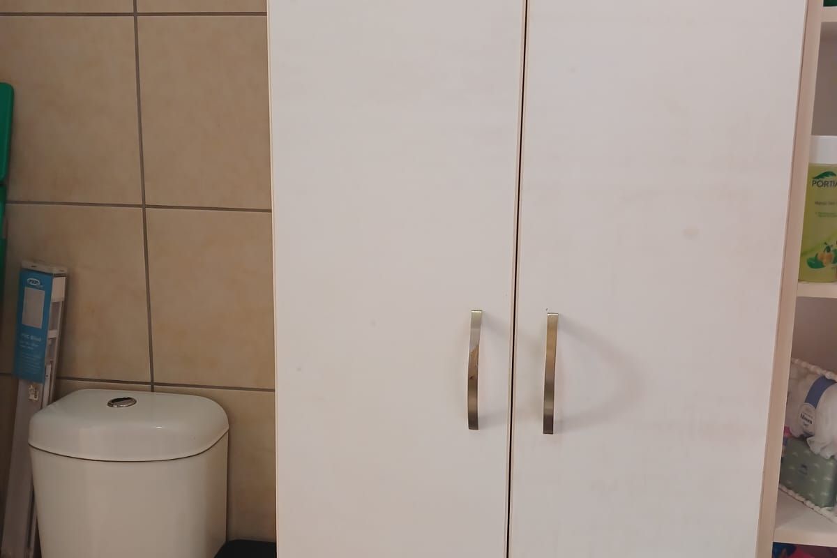 A functional bathroom featuring a standard toilet and a tall, white built-in storage cupboard with modern handles against tiled walls.