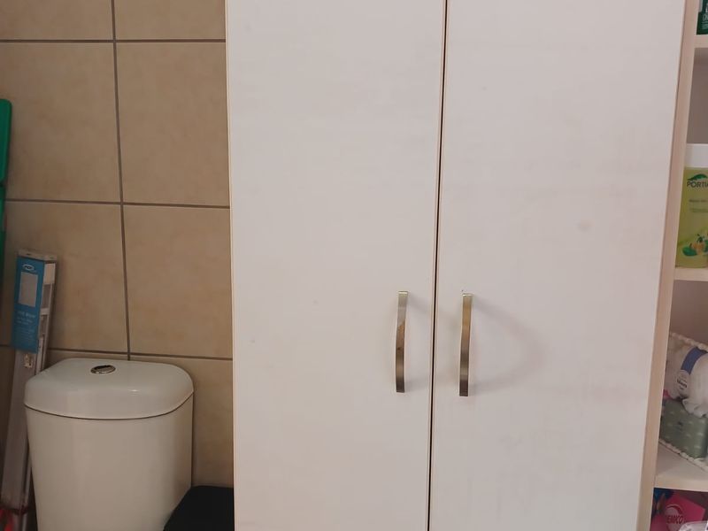 A functional bathroom featuring a standard toilet and a tall, white built-in storage cupboard with modern handles against tiled walls.