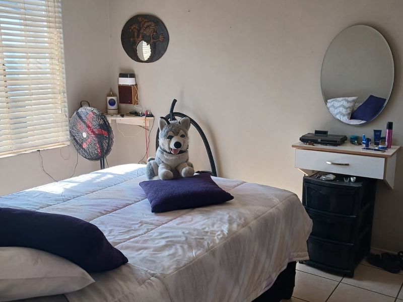 A bedroom featuring tiled flooring, a ceiling fan, and a wall-mounted vanity unit with a mirror.