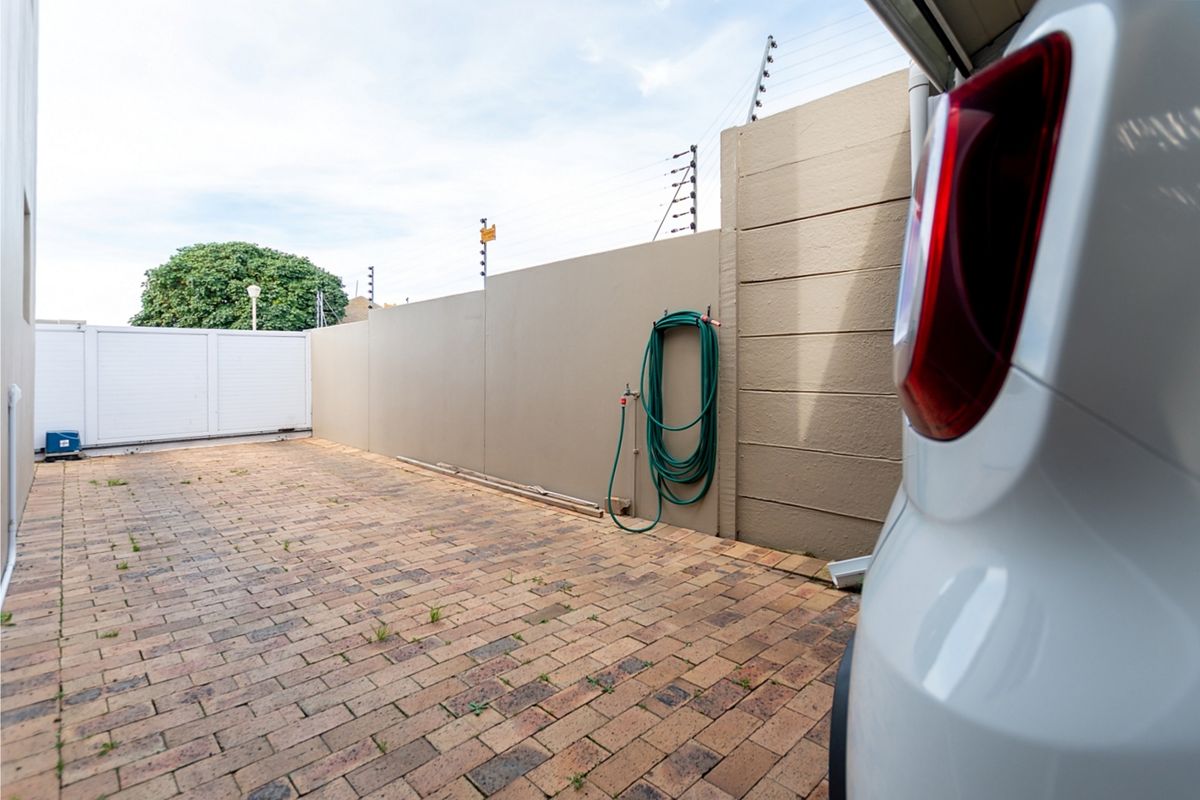 A paved rear courtyard area featuring a high boundary wall with electric fencing and a sliding gate entrance.