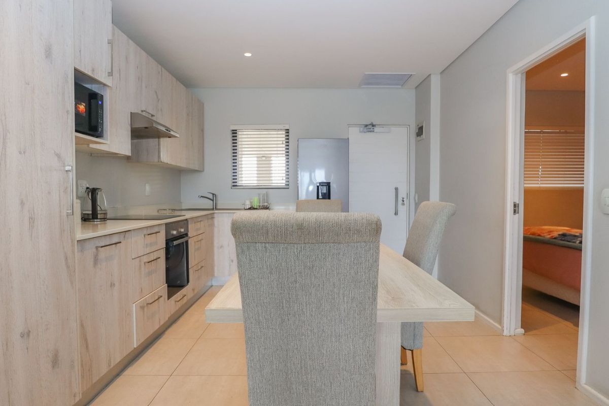 Modern kitchen featuring light wood-finish cabinetry, integrated appliances, and tiled flooring, seamlessly flowing into the adjacent dining area.
