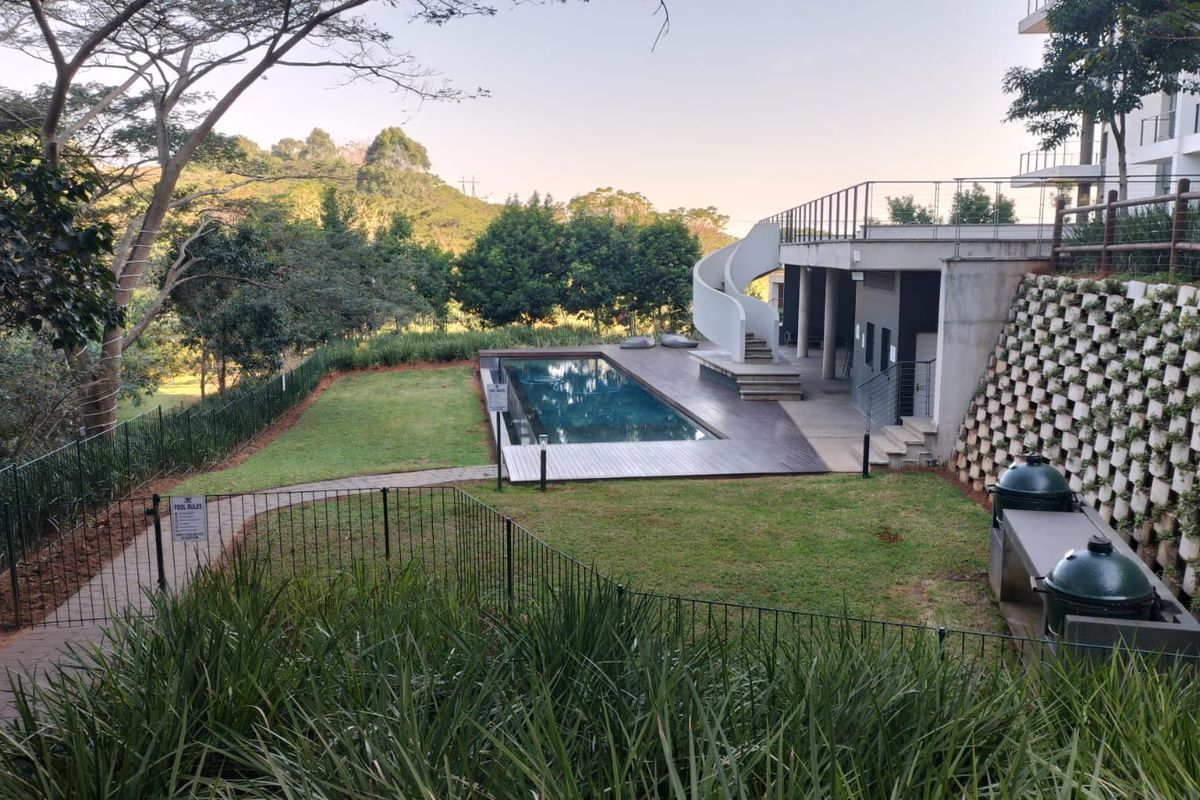 Communal pool area featuring a swimming pool, timber decking, spiral staircase, and built-in braai facilities set within a landscaped garden.