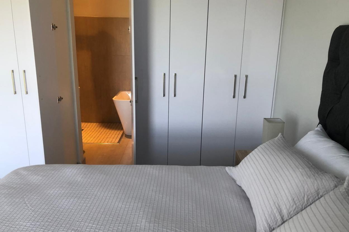 A well-maintained bedroom featuring built-in cupboards and direct access to an en-suite bathroom equipped with a shower and freestanding bathtub.