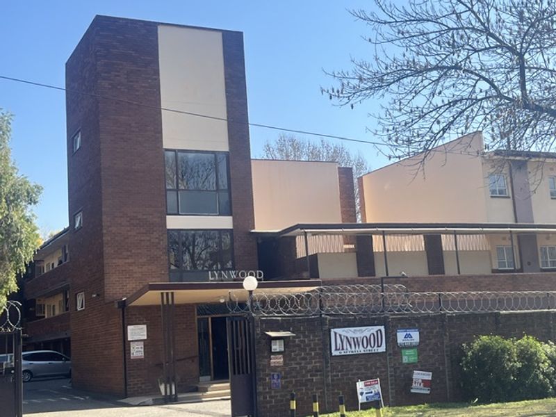 Front exterior view of the Lynwood apartment complex featuring brick facade, secure gated entrance, and perimeter security fencing.