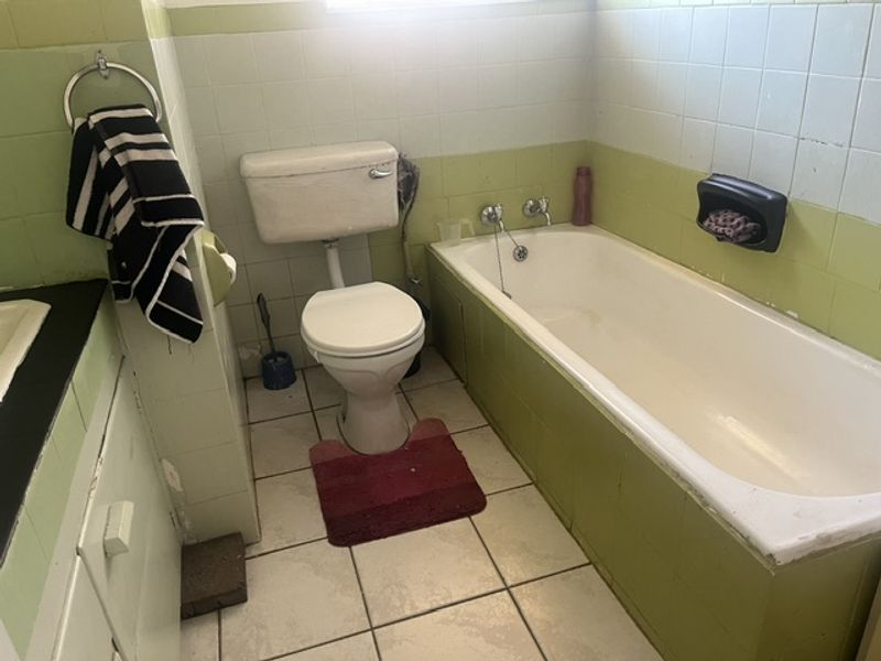 A dated bathroom featuring a standard bathtub, toilet, and tiled finishes, offering significant potential for a modern renovation.
