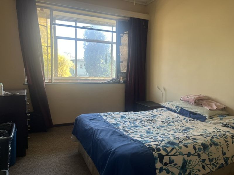 A bedroom featuring carpet flooring and a large window with natural light, currently requiring cosmetic updates to the walls and window fixtures.