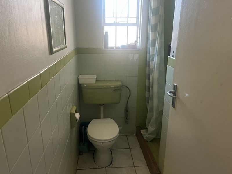A compact bathroom featuring dated green and white wall tiling, a standard toilet, and a shower area with a curtain.