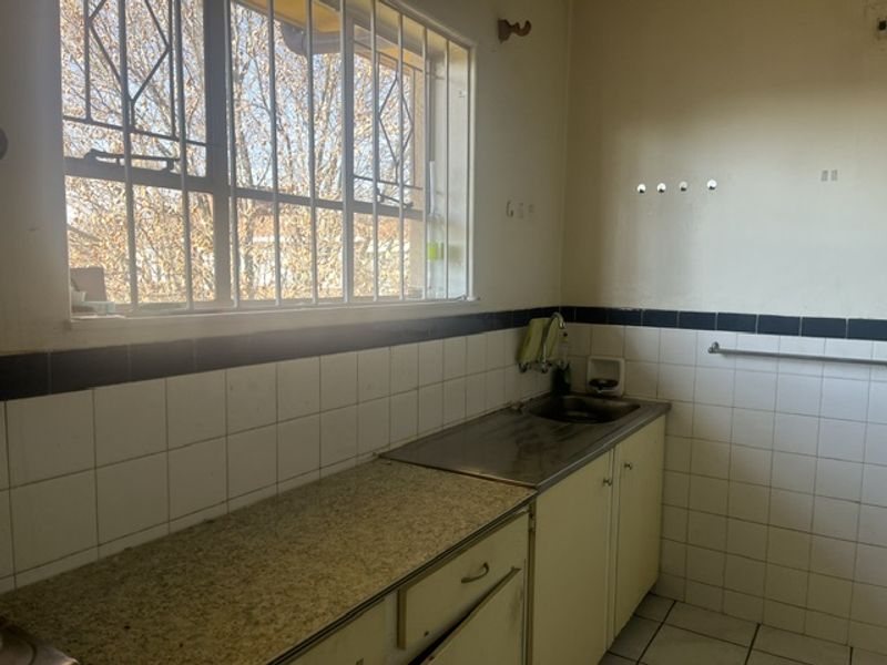 A functional kitchen space featuring a stainless steel sink, laminate countertops, and tiled backsplash, currently vacant and ready for renovation.
