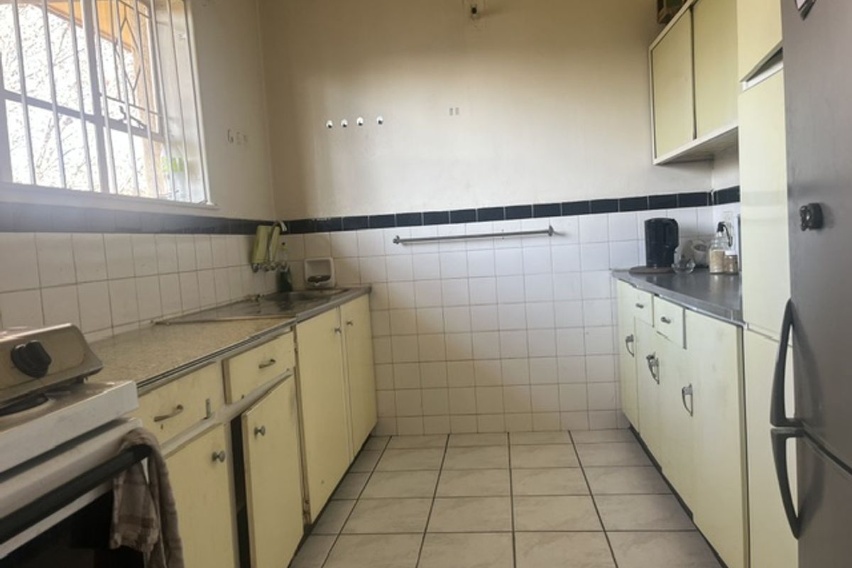 A functional kitchen featuring dated cabinetry, tiled backsplash, and tiled flooring, offering potential for modernization and renovation.