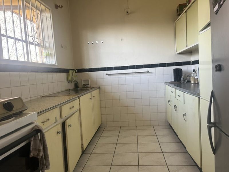 A functional kitchen featuring dated cabinetry, tiled backsplash, and tiled flooring, offering potential for modernization and renovation.