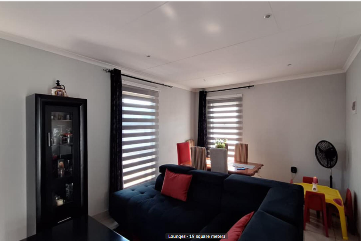 A well-lit living area featuring neutral walls, recessed ceiling lighting, and dual-aspect windows with modern roller blinds and curtain rods.