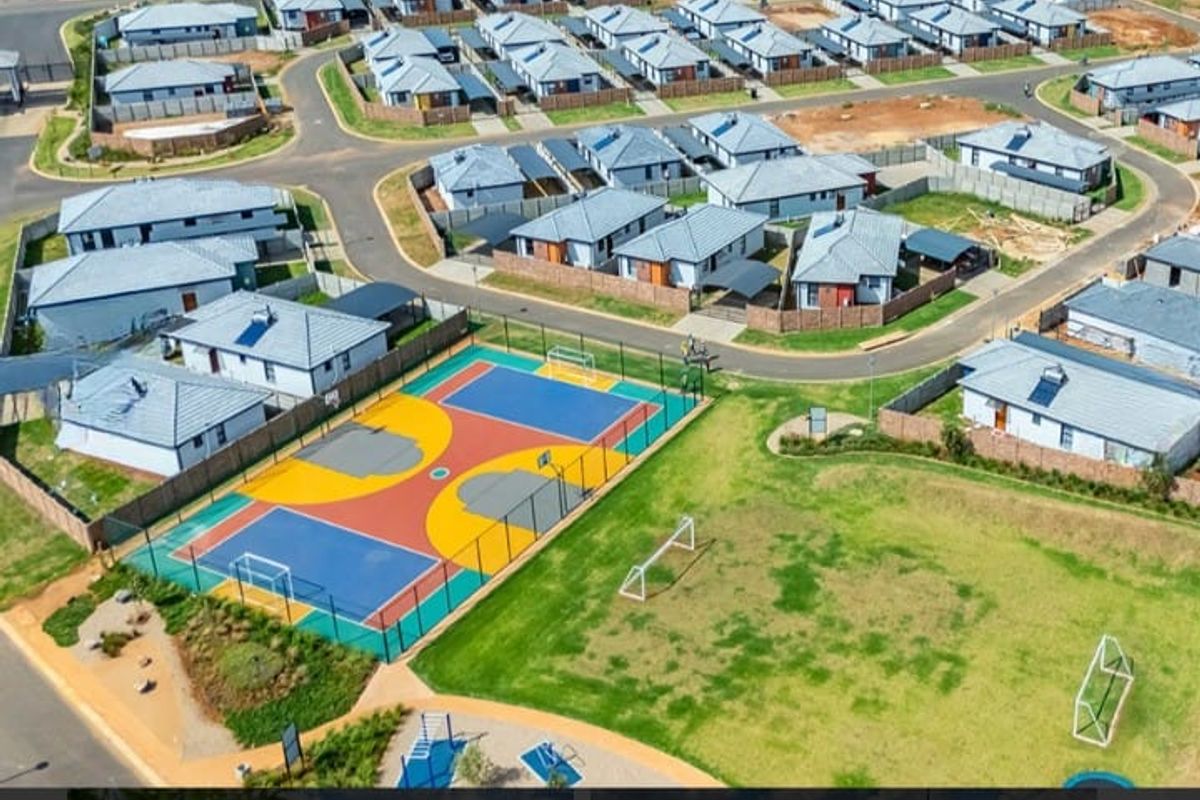 Aerial view of a residential estate featuring a multi-purpose sports court, landscaped green spaces, and surrounding modern housing units.