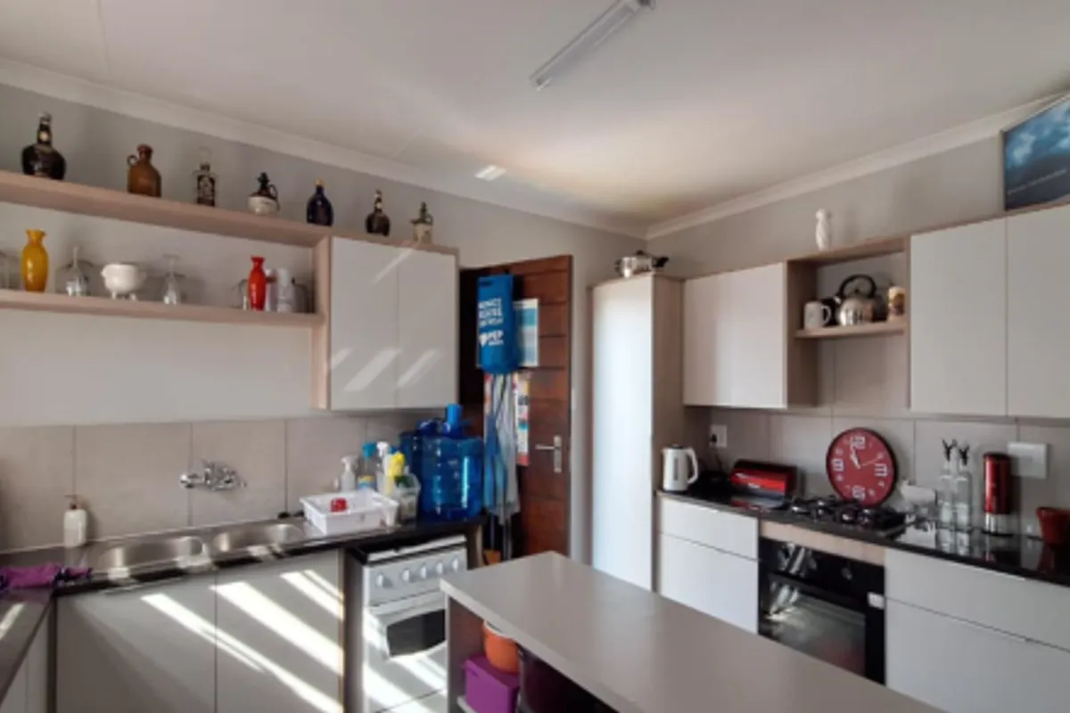 A functional kitchen featuring modern white cabinetry, dark countertops, a built-in oven, gas hob, and a stainless steel double sink with tiled backsplash.