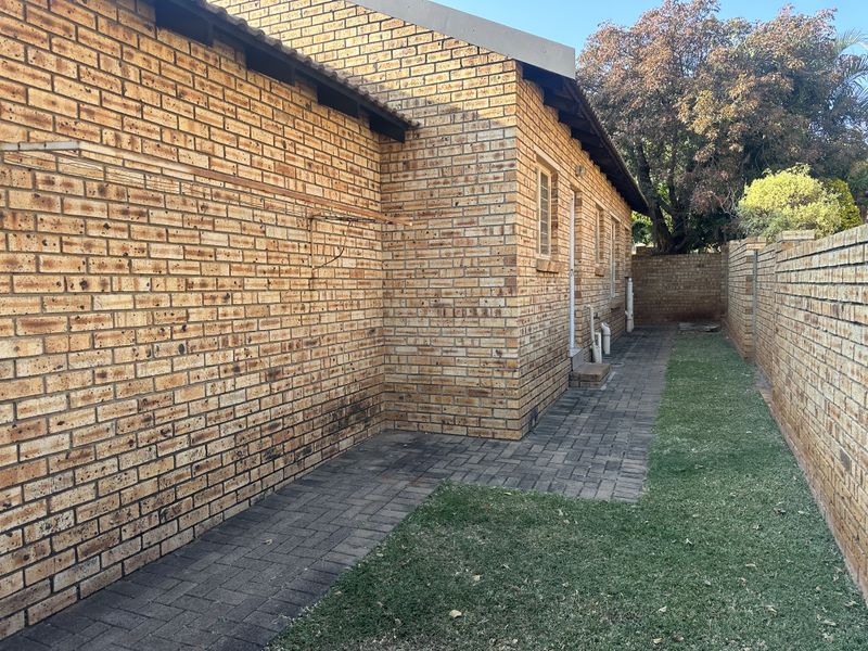 A view of the rear exterior of the house featuring face brick walls, a paved walkway, and a brick boundary wall.