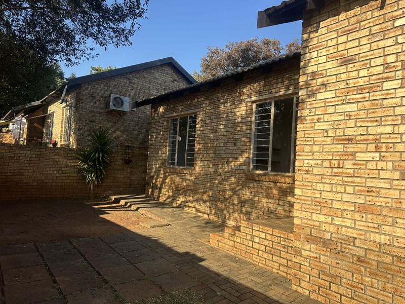 A rear exterior view of a face brick house featuring a paved patio area and security bars on the windows.
