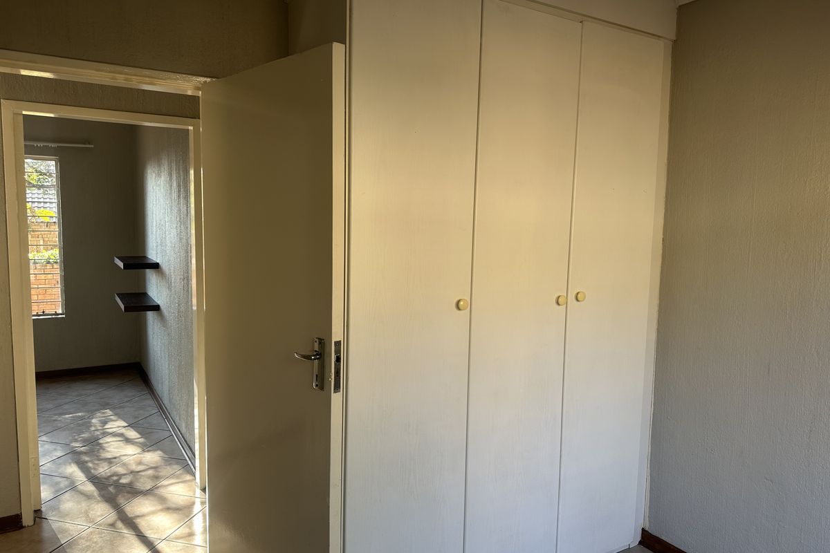 A clean, empty bedroom featuring built-in cupboards and tiled flooring, with a view into an adjacent hallway.