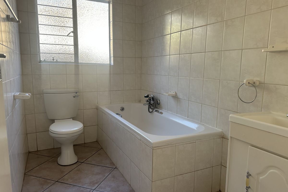 A functional bathroom featuring a bathtub, toilet, and vanity basin with tiled walls and flooring, offering a clean, dated aesthetic ready for modernization.