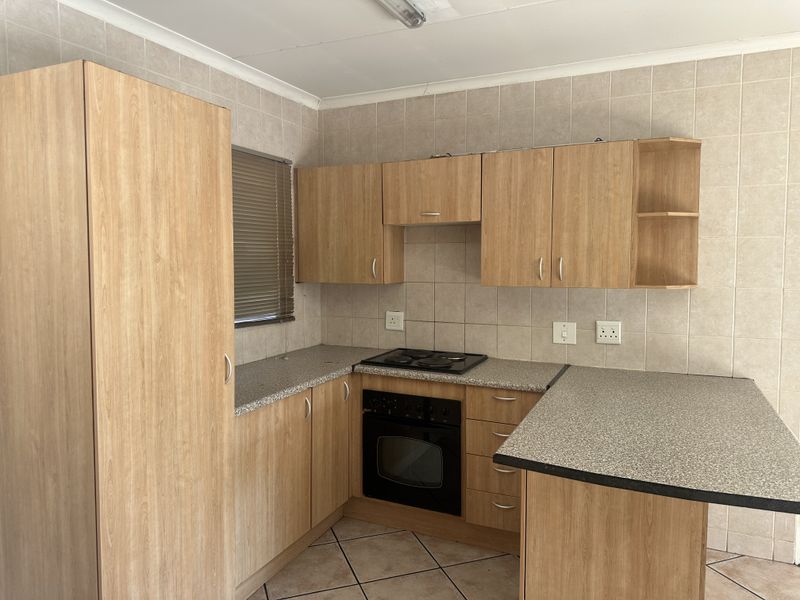 A functional kitchen featuring light wood-finish cabinetry, laminate countertops, a built-in oven and hob, and neutral tiled wall finishes.