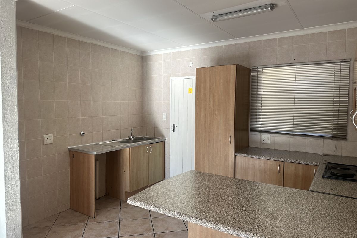 A functional kitchen featuring built-in cabinetry, laminate countertops, a stainless steel sink, and tiled finishes throughout.