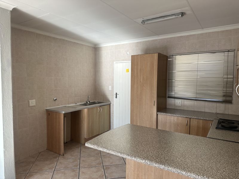 A functional kitchen featuring built-in cabinetry, laminate countertops, a stainless steel sink, and tiled finishes throughout.