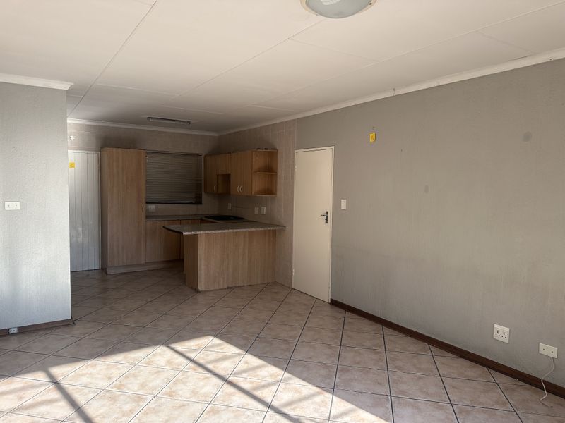 An open-plan living and kitchen area featuring tiled flooring, built-in wooden cabinetry, and a breakfast counter, offering a blank canvas for personalization.