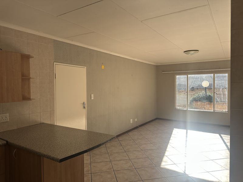 An open-plan living and kitchen area featuring tiled flooring, a breakfast counter, and natural light from a large window.