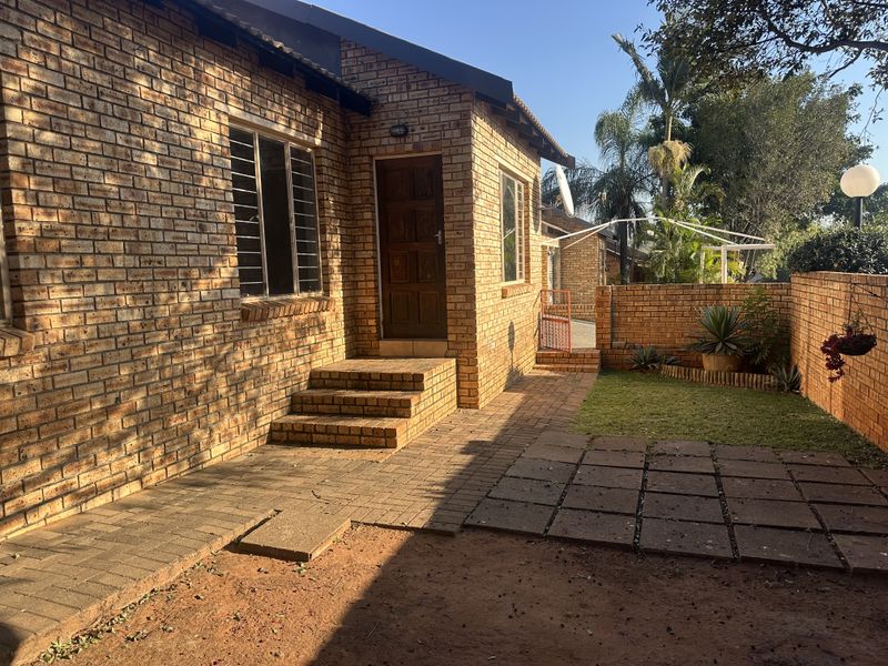 A rear exterior view of a face brick house featuring a paved patio area, brick steps, and a small private garden with boundary walls.