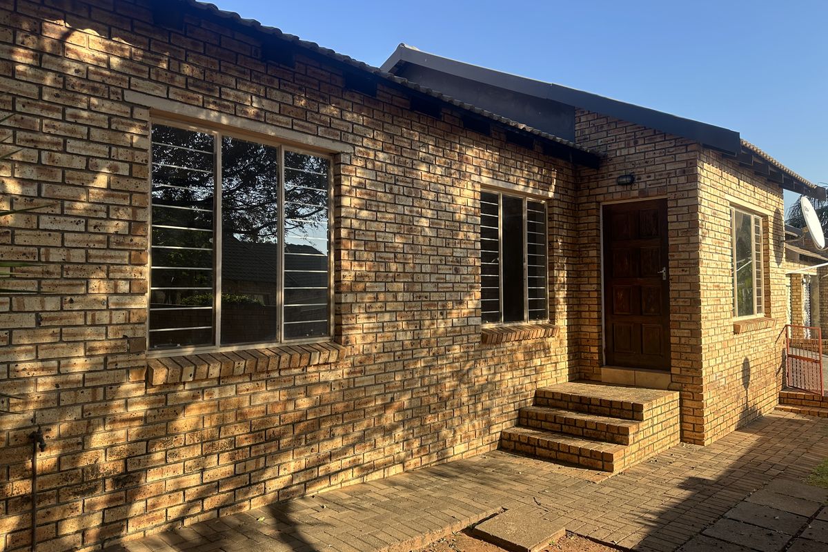 A rear exterior view of a face brick house featuring a paved patio area, brick steps, and security bars on the windows.