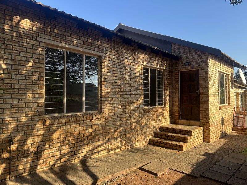 A rear exterior view of a face brick house featuring a paved patio area, brick steps, and security bars on the windows.