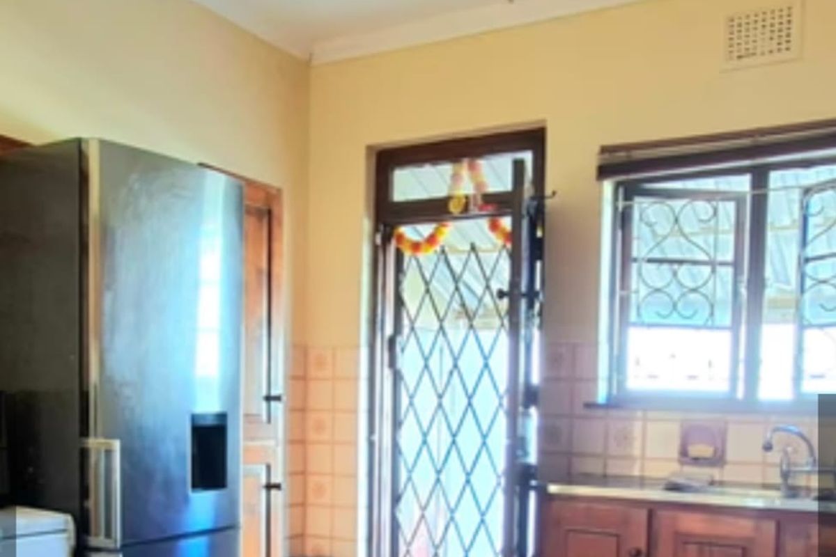 A functional kitchen featuring wooden cabinetry, tiled backsplash, and tiled flooring, with direct access to the exterior through a security gate.