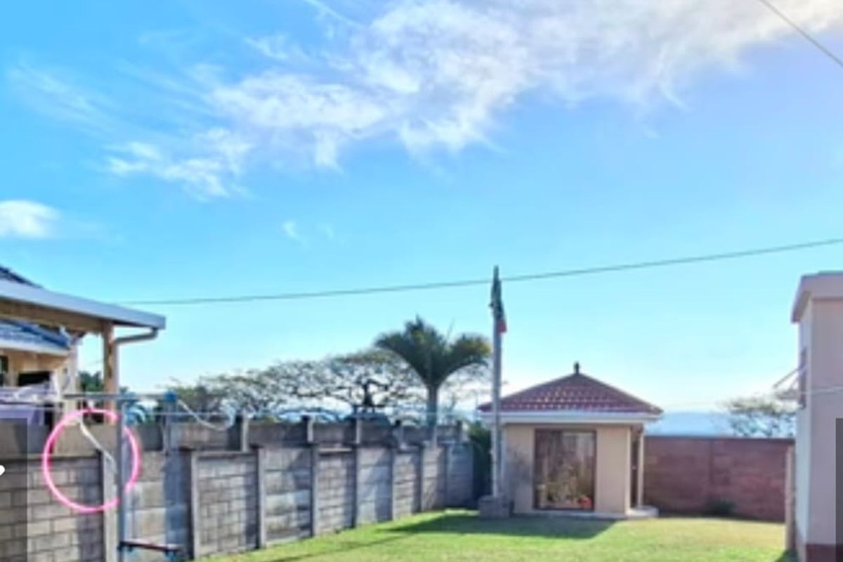 A spacious rear garden featuring a lawn, concrete block boundary wall, and a small detached outbuilding with a tiled roof.
