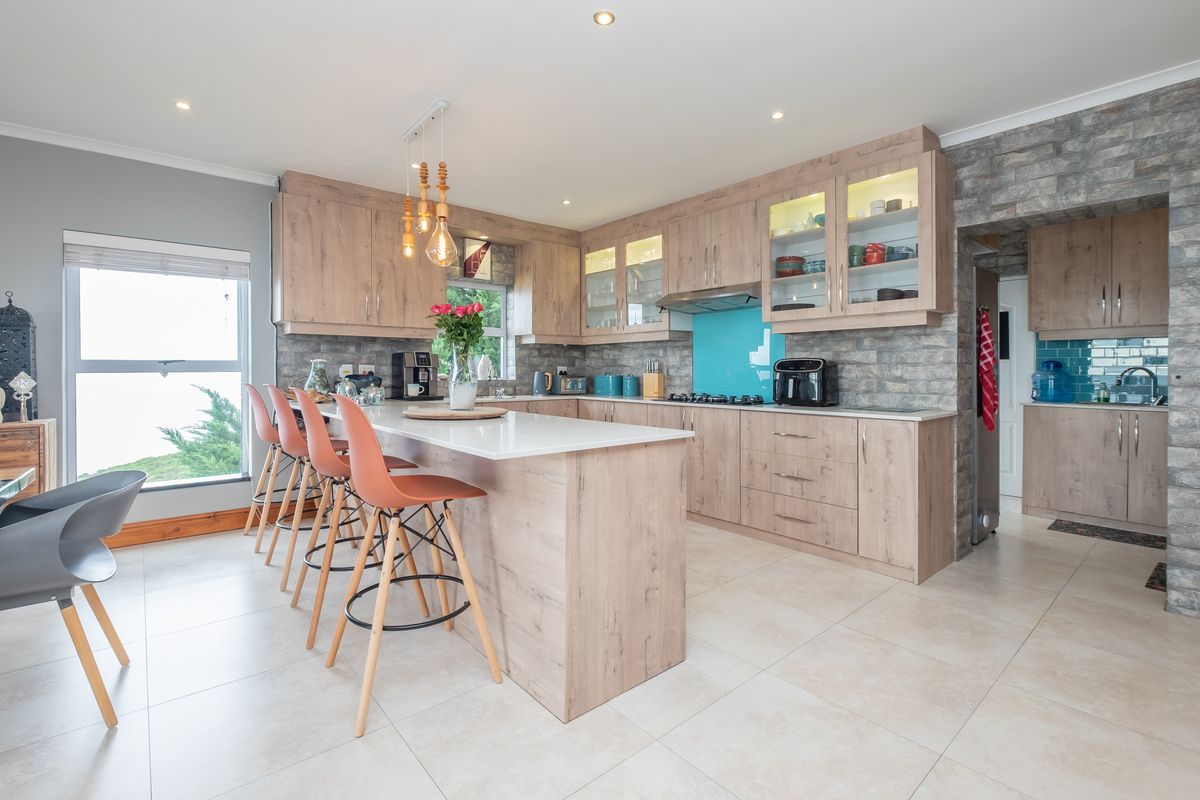 Modern kitchen featuring light wood cabinetry, a central island with breakfast bar, stone veneer accents, and an adjoining scullery area.