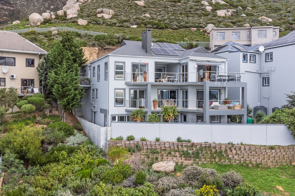 Rear elevation of a multi-story residential property featuring tiered balconies, solar panels, and a landscaped retaining wall against a mountain backdrop.