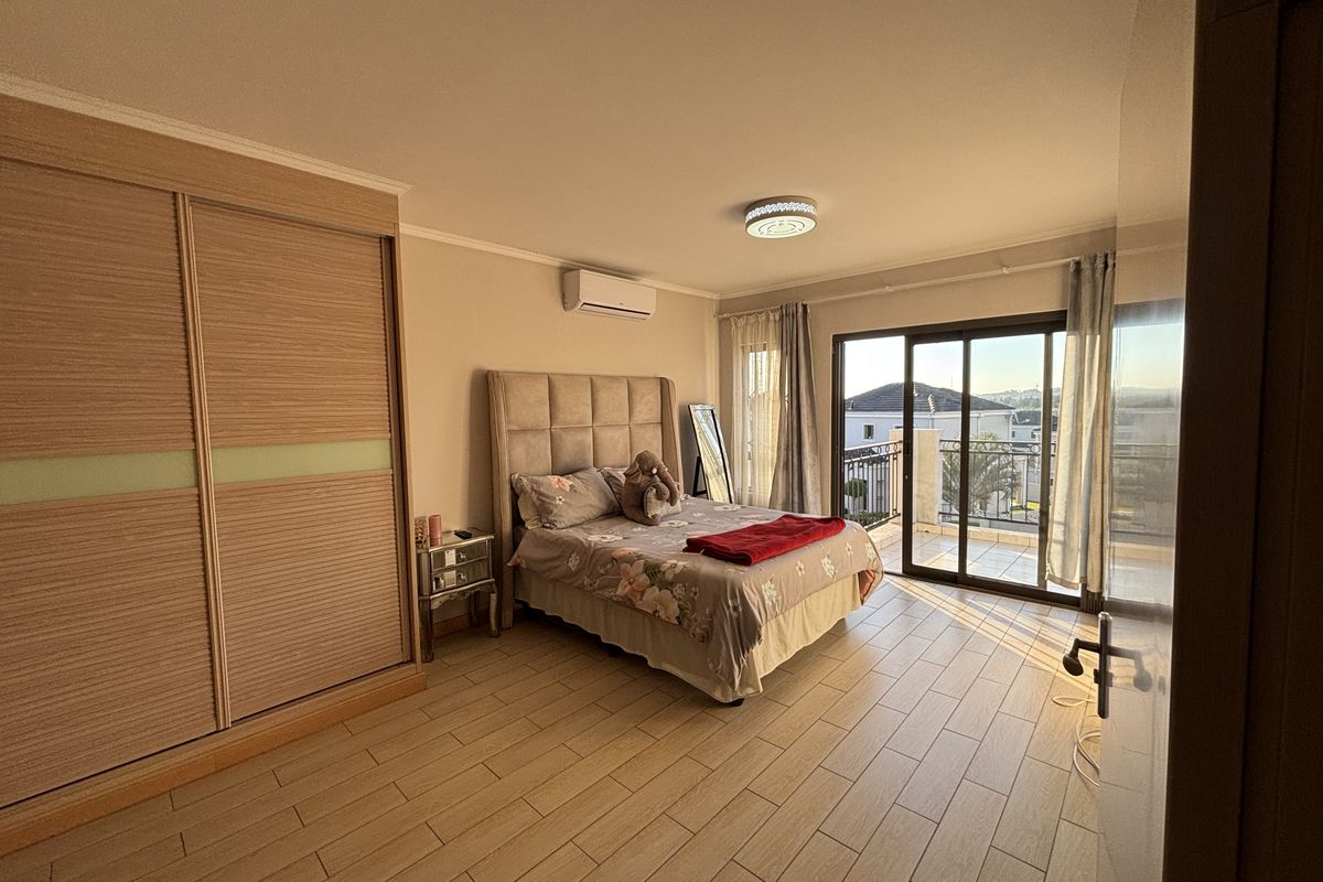 Spacious bedroom featuring wood-look tiled flooring, a large built-in sliding wardrobe, split-system air conditioning, and direct access to a private balcony.