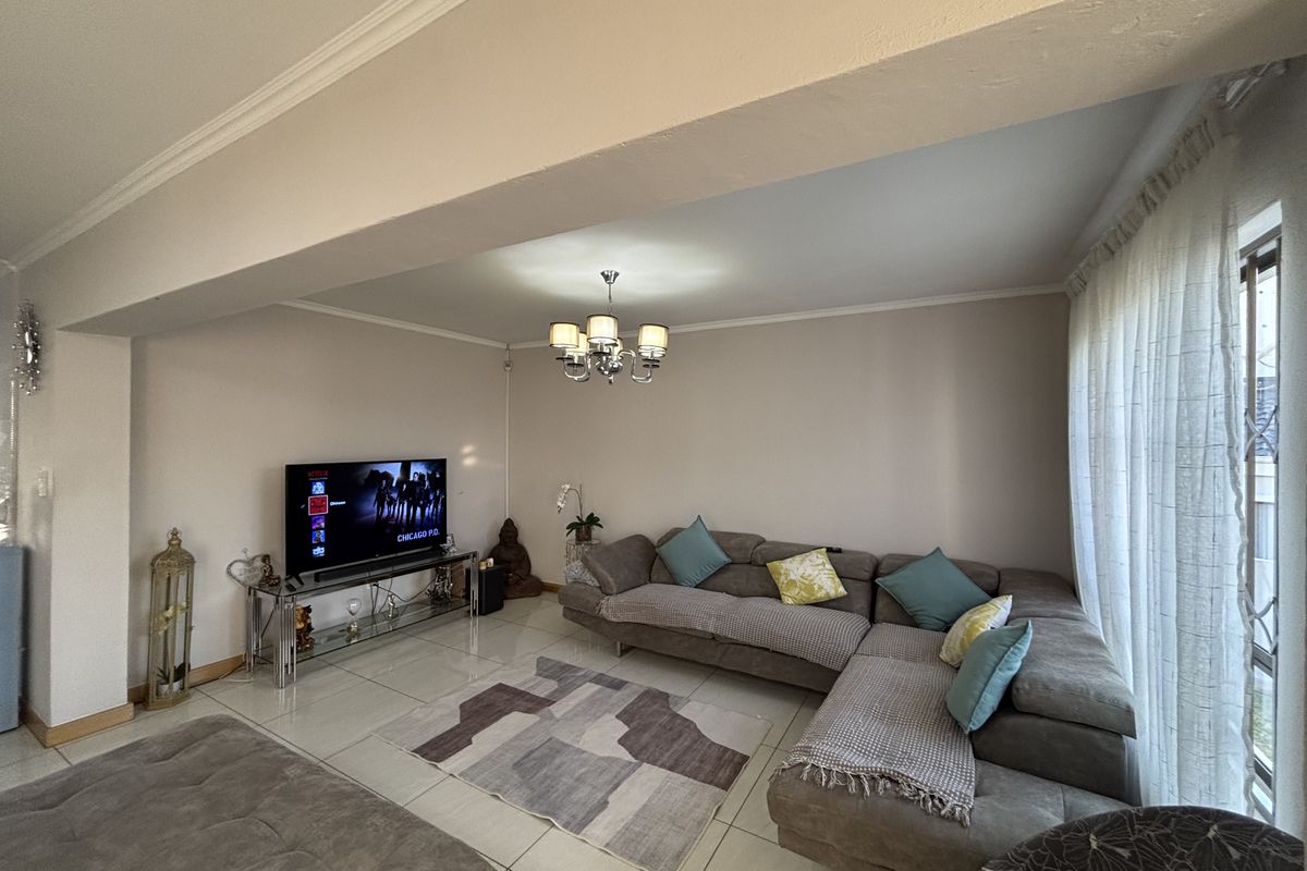 A well-maintained living room featuring polished porcelain floor tiles, decorative cove ceiling molding, and a central chandelier, offering a bright and comfortable living space.