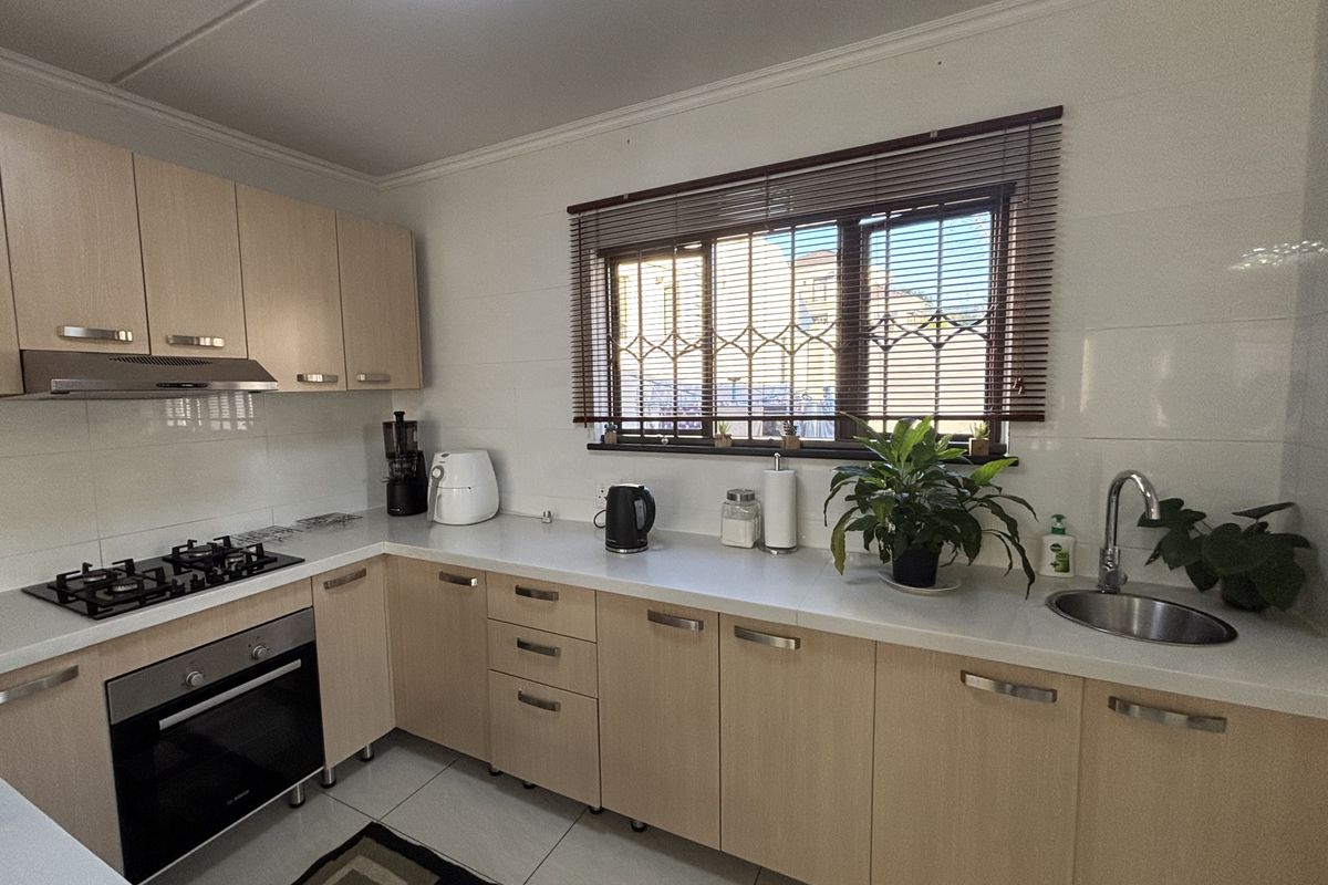 A functional kitchen featuring light wood cabinetry, a gas hob with extractor, built-in oven, and a stainless steel sink with tiled surfaces.