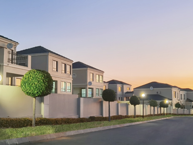 A scenic street view of a modern residential cluster estate at sunset, featuring well-maintained boundary walls, paved roads, and uniform architectural styling.