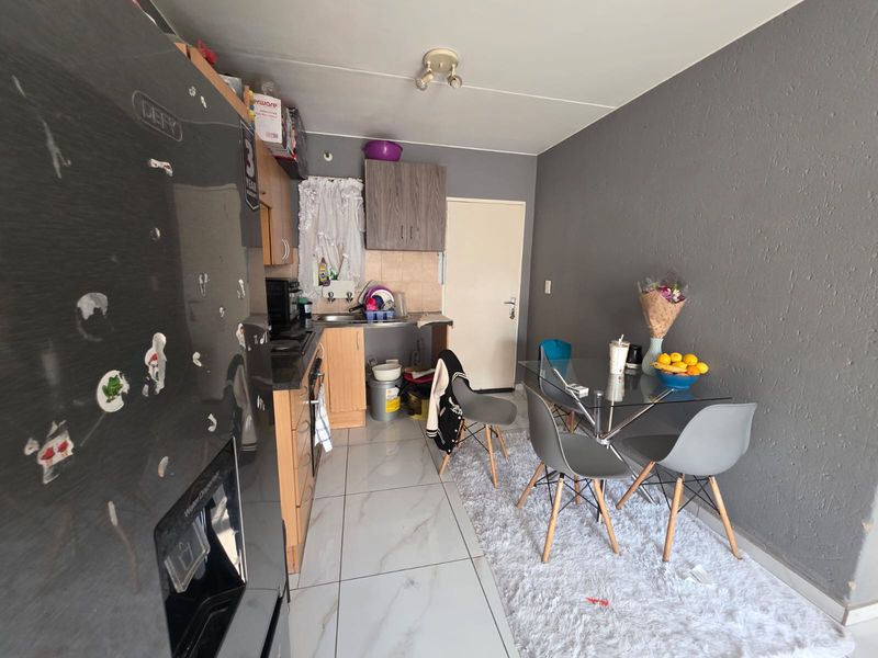 An open-plan kitchen and dining area featuring tiled flooring, wooden cabinetry, and a functional layout suitable for compact apartment living.