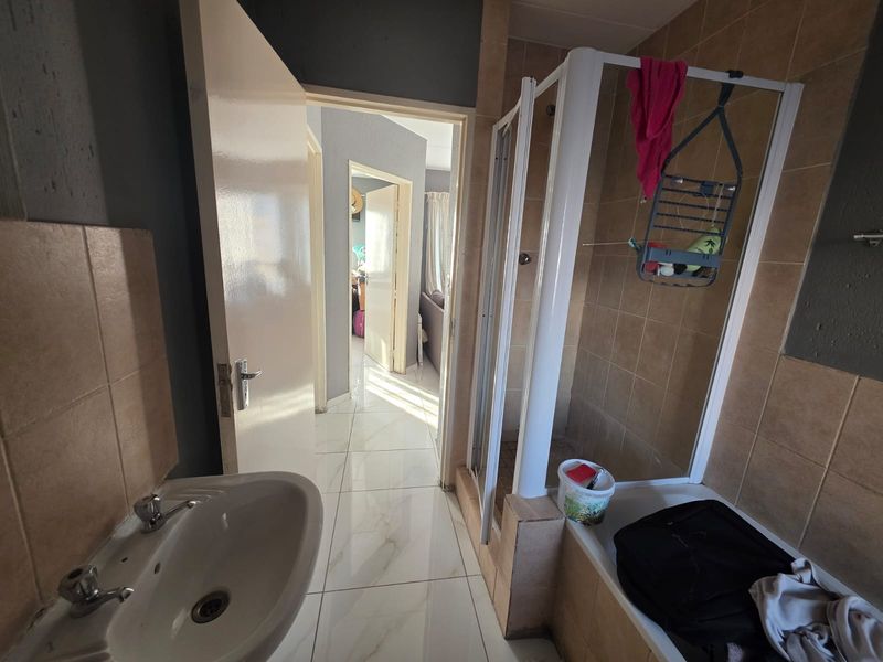A functional bathroom featuring a shower enclosure, pedestal basin, and tiled finishes, connecting to a hallway area.